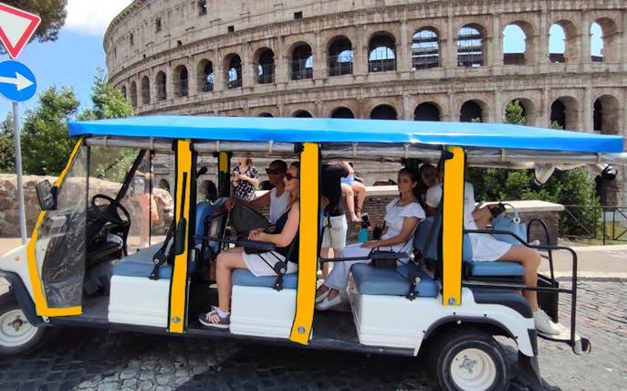 Electric golf cart with tourists near the Colosseum in Rome.