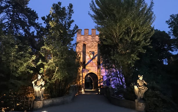 Entrance of Gropparello Castle illuminated at night, surrounded by trees and statues.