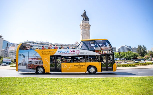 Open-top yellow bus on Porto Vintage Bus Tour passing a monument in a city square.