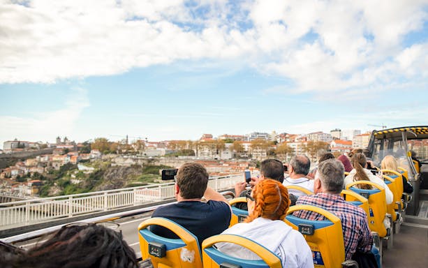 Tourists on an open-top bus capturing views of Porto's cityscape.