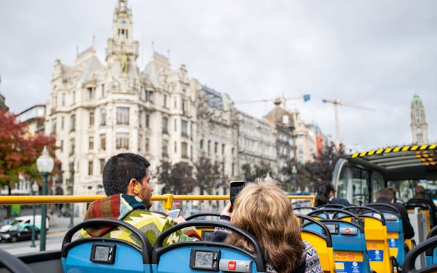 Open-top bus tour in Porto passing by historic architecture.