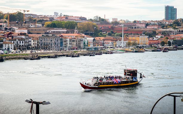 Vintage boat cruising on Douro River with Porto cityscape in the background.