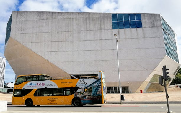 Yellow double-decker bus in front of Casa da Música, Porto, for hop-on hop-off tour.