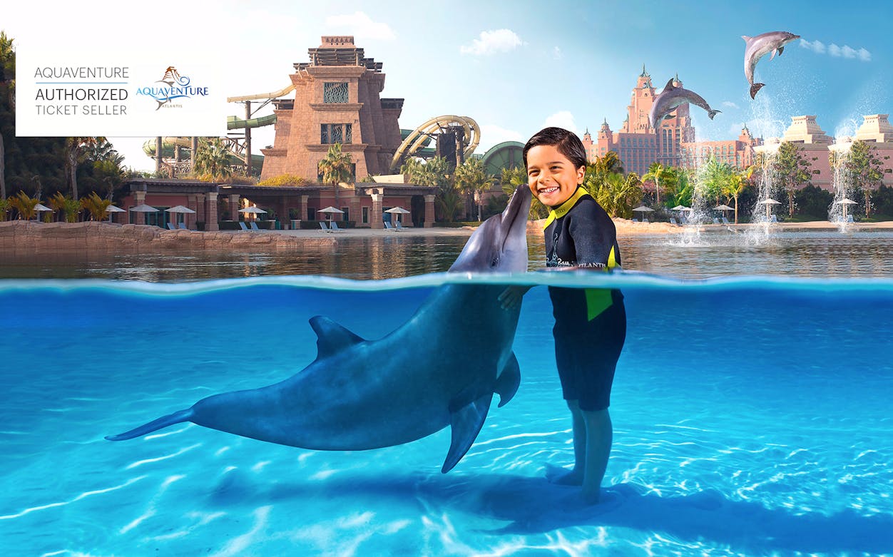 Child interacting with a dolphin at Aquaventure Waterpark, Atlantis, with slides and fountains in the background.