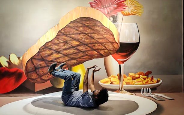 Person interacting with 3D art of steak and wine at Illusion 3D Art Museum Melaka.