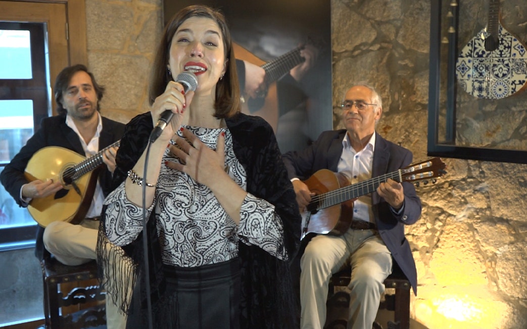 Fado singer performing with guitarists in a Port wine cellar concert.
