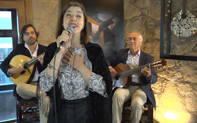 Fado singer performing with guitarists in a Port wine cellar concert.