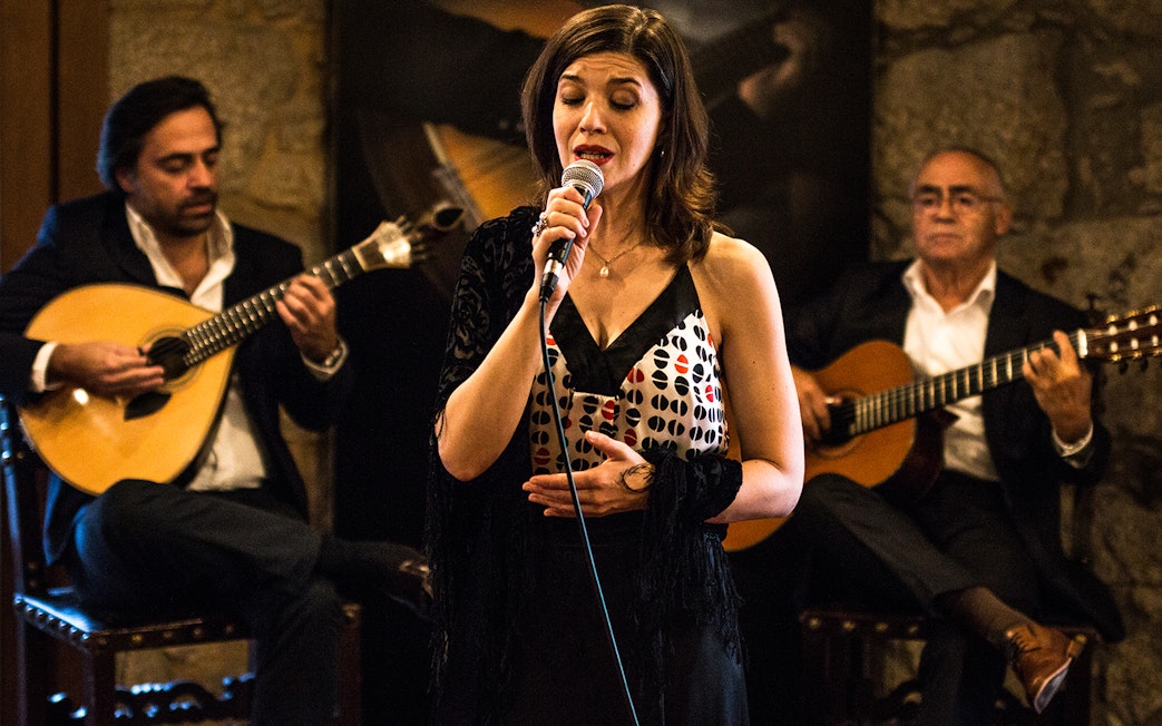 Fado singer performing with guitarists in a Port wine cellar.