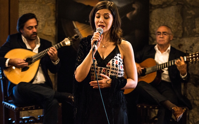 Fado singer performing with guitarists in a Port wine cellar.