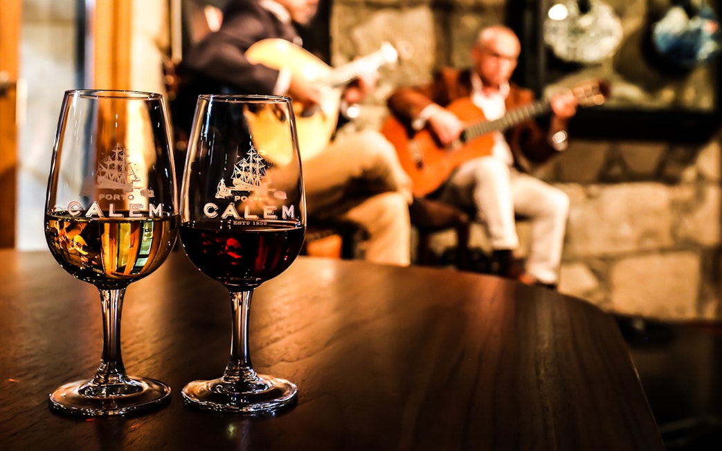 Fado musicians performing in a Port wine cellar with glasses of wine in the foreground.