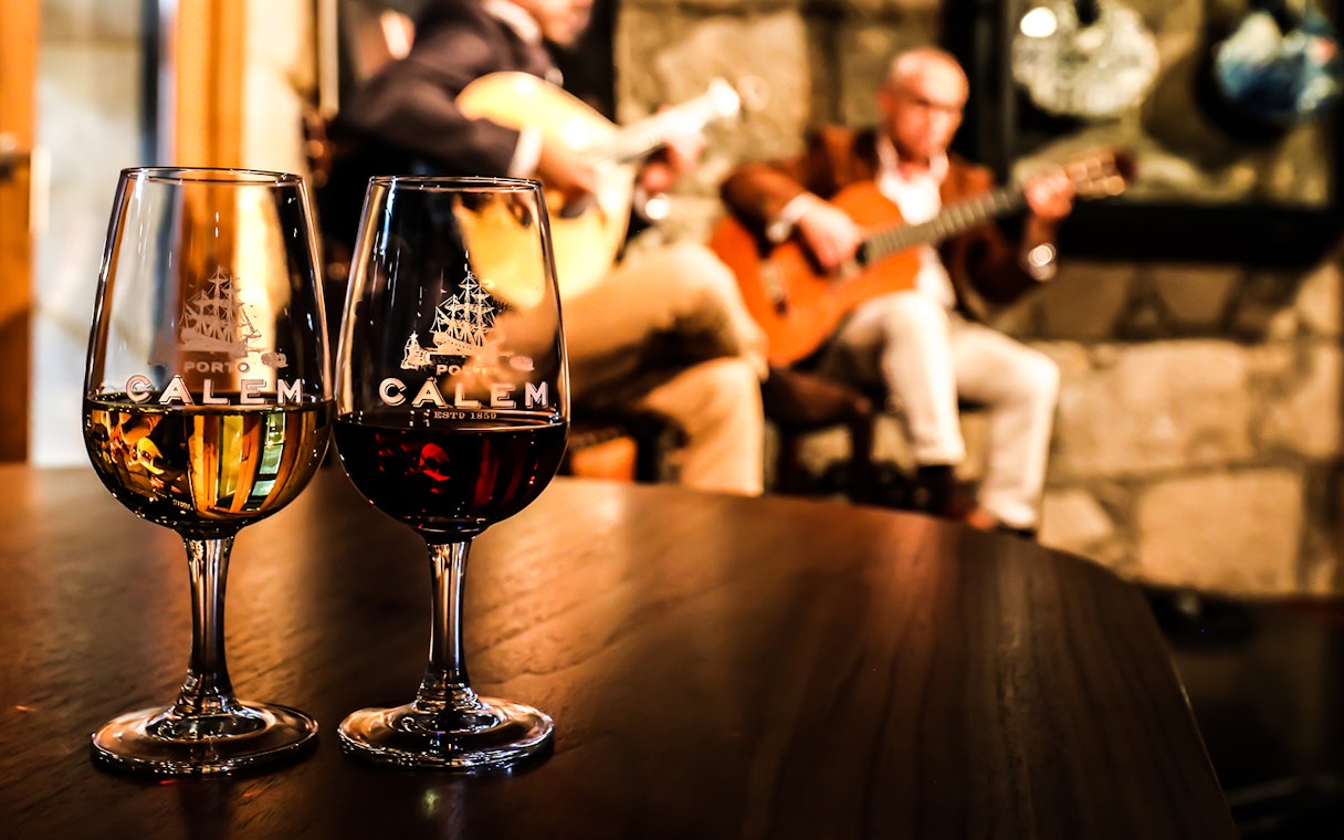 Fado musicians performing in a Port wine cellar with glasses of wine in the foreground.