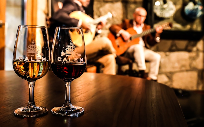 Fado musicians performing in a Port wine cellar with glasses of wine in the foreground.