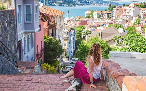 Woman sitting on steps overlooking Istanbul cityscape with Bosphorus view.