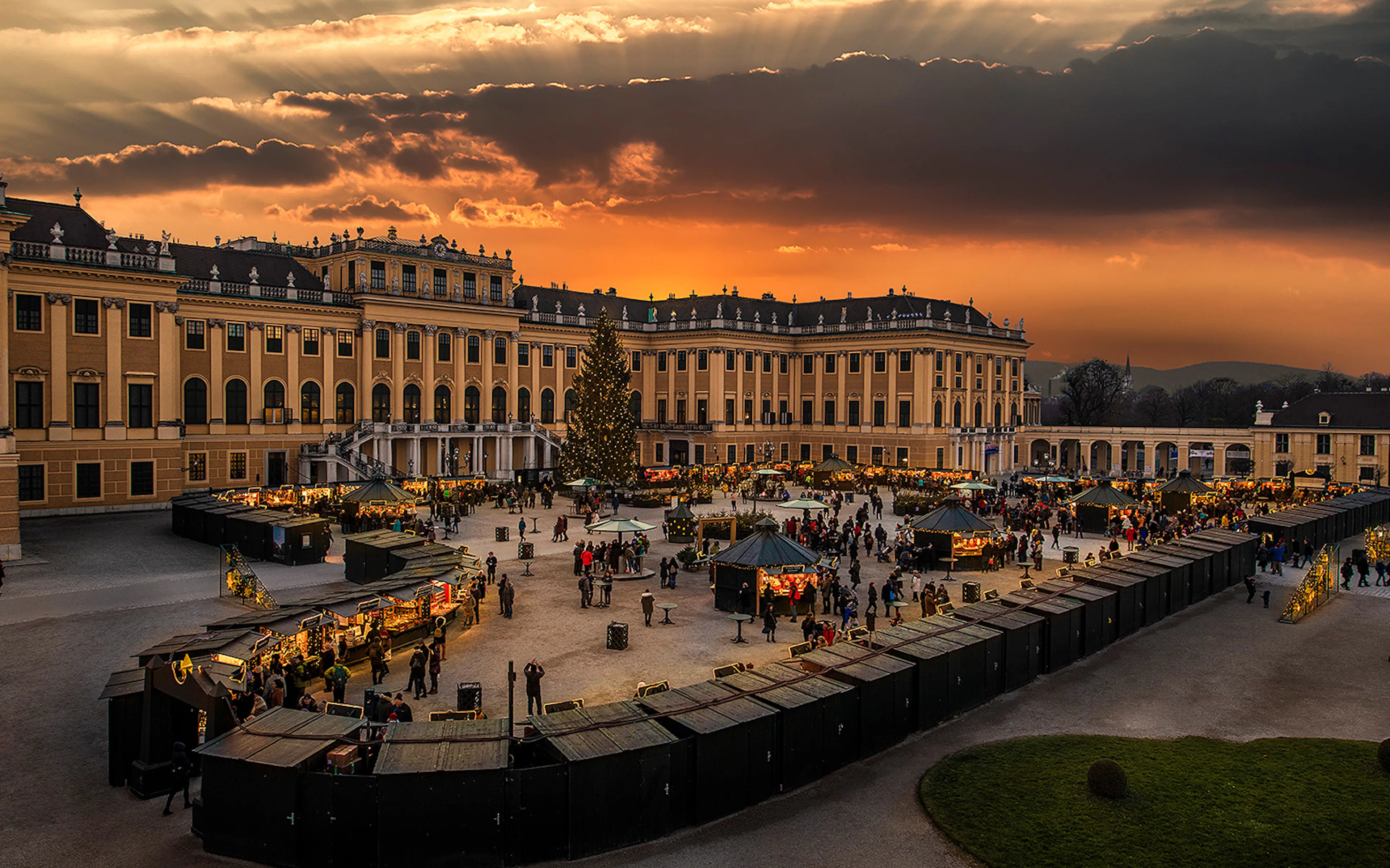 Schönbrunn Palace Christmas Market at sunset with festive stalls and visitors.