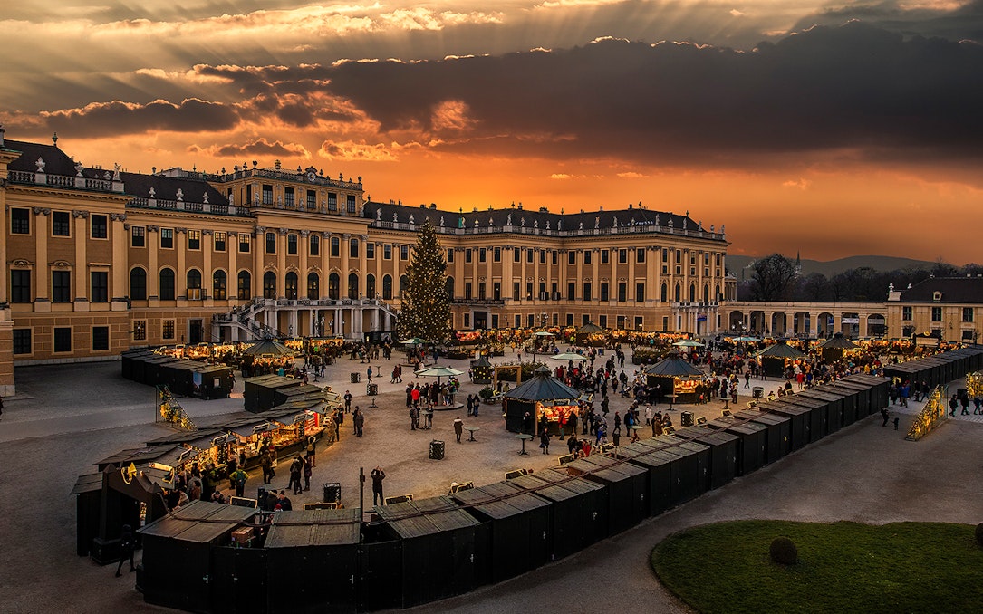 Schönbrunn Palace Christmas Market at sunset with festive stalls and visitors.