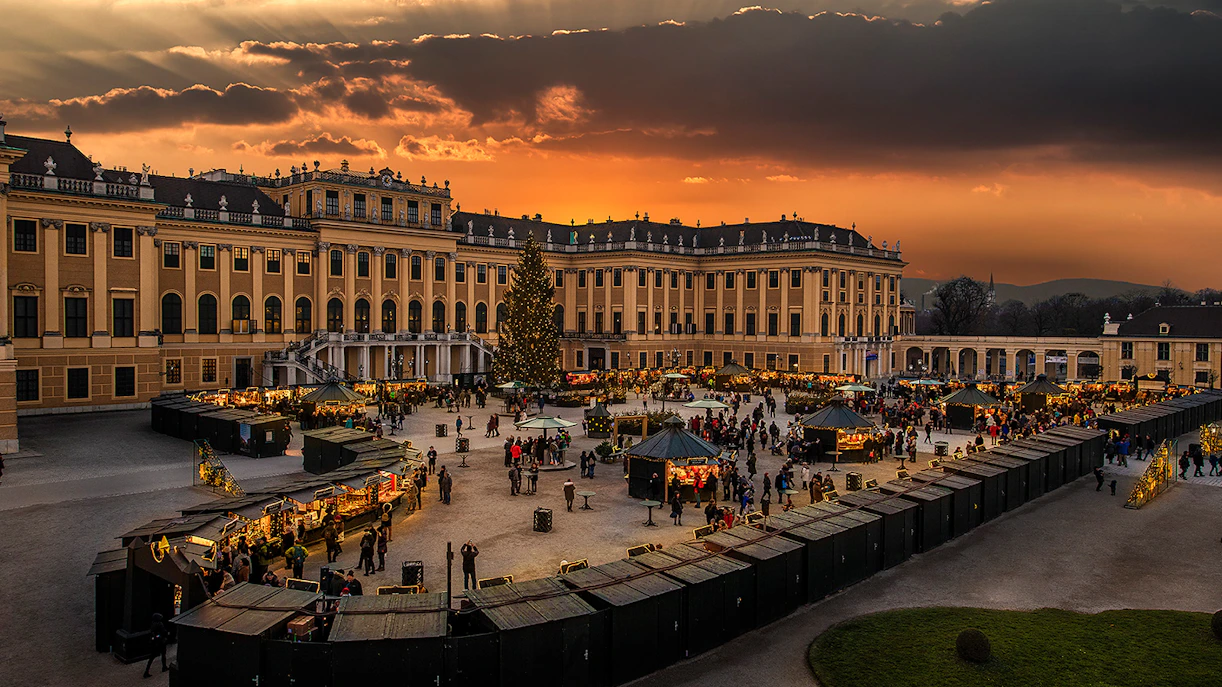 Schönbrunn Palace Christmas Market at sunset with festive stalls and visitors.