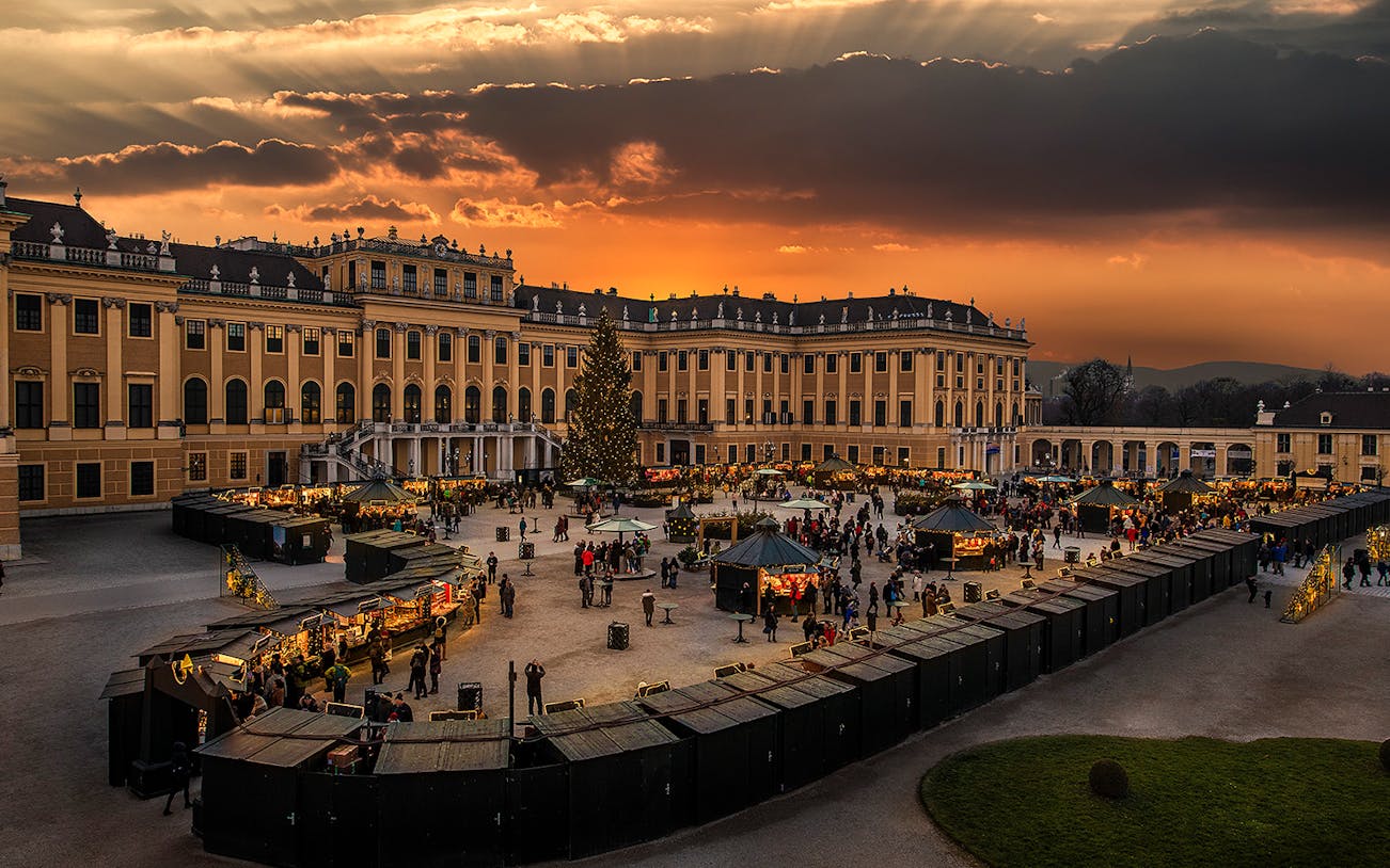Schönbrunn Palace Christmas Market at sunset with festive stalls and visitors.