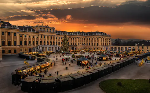 Schönbrunn Palace Christmas Market at sunset with festive stalls and visitors.