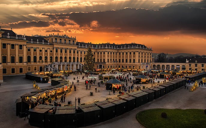 Schönbrunn Palace Christmas Market at sunset with festive stalls and visitors.