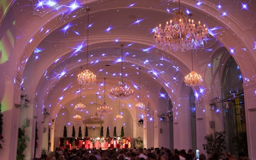 Concert hall at Schönbrunn Palace with chandeliers and festive lighting during Mozart & Strauss performance.