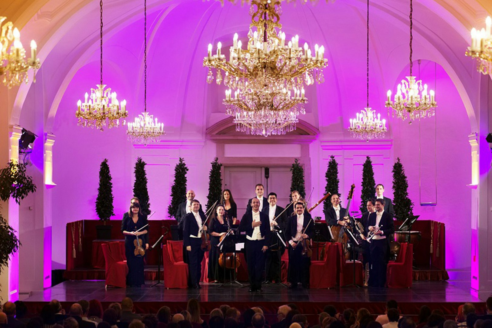 Orchestra performing at Schönbrunn Palace with chandeliers and festive decor.
