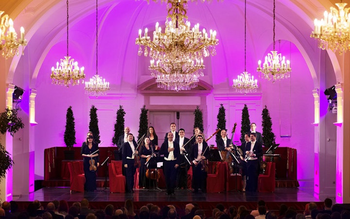 Orchestra performing at Schönbrunn Palace with chandeliers and festive decor.