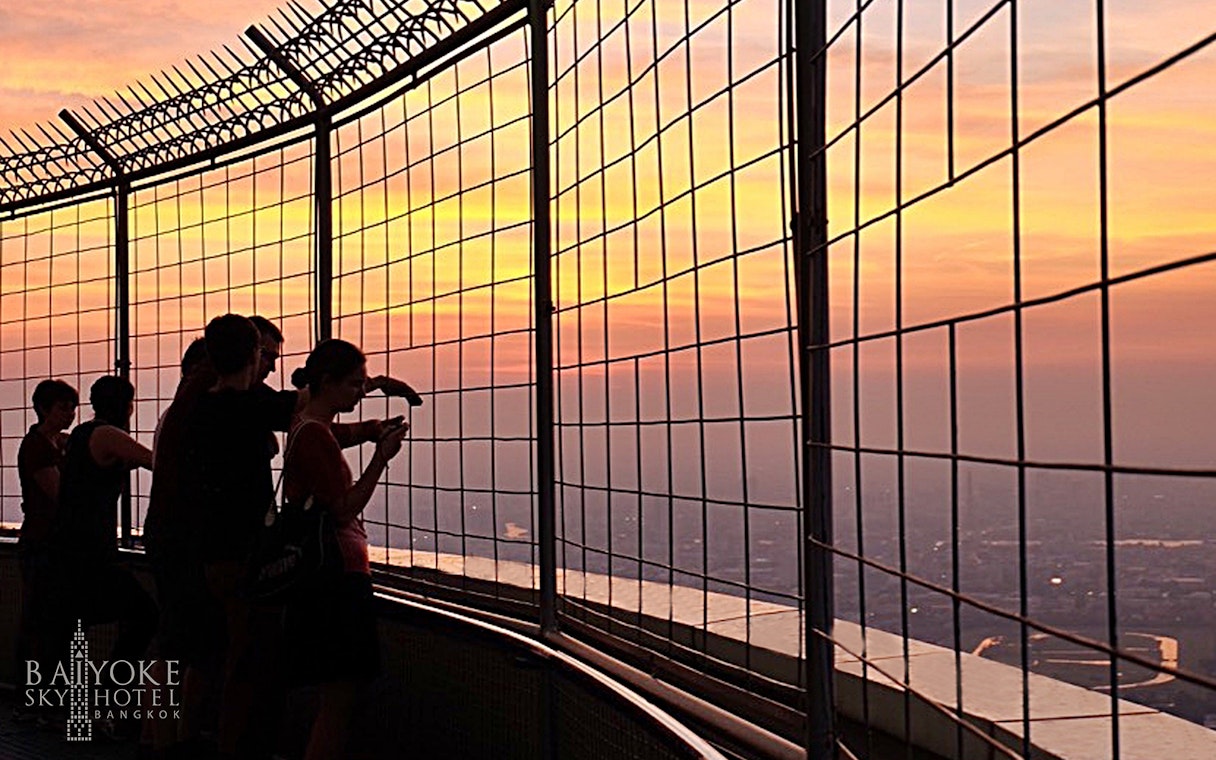 Visitors at Baiyoke Sky Hotel Observatory enjoying sunset views over Bangkok.
