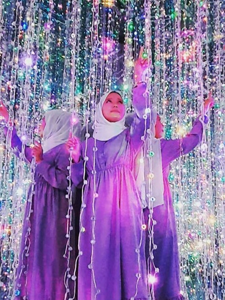 Tourist interacting with light display in starlight room at selfie museum.