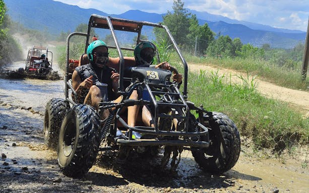 Two people driving an off-road buggy through muddy terrain in Koprulu Canyon.
