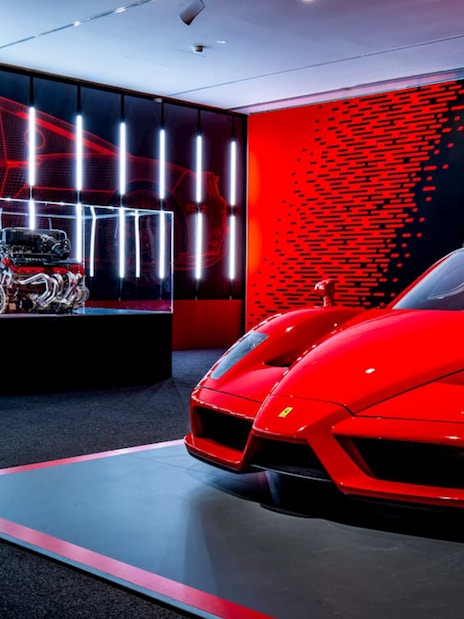 Ferrari Enzo displayed at Ferrari Museum Maranello with engine exhibit in background.