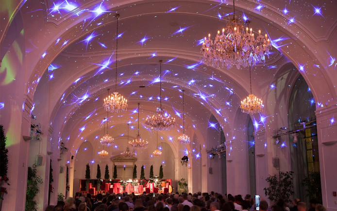 Concert audience in Schönbrunn Palace hall with chandeliers and starry light display.