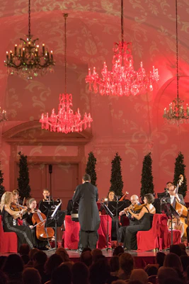 Orchestra performing at Schönbrunn Palace concert hall with chandeliers and red lighting.