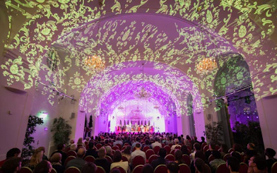 Concert audience in Schönbrunn Palace with ornate ceiling projections.