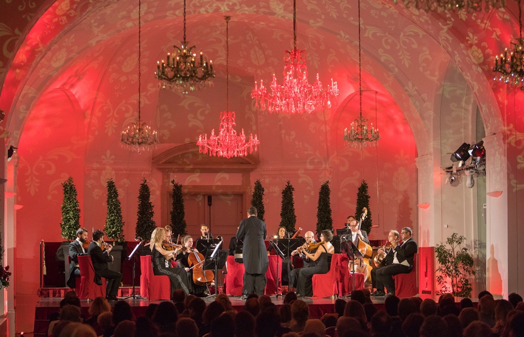 Rot erleuchteter Saal im Schloss Schönbrunn mit Orchester auf der Bühne und Publikum