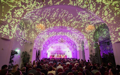 Concert audience in Schönbrunn Palace with ornate ceiling projections during Mozart & Strauss performance.