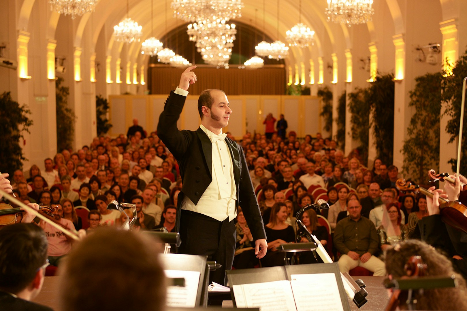 Conductor leading orchestra at Schönbrunn Palace concert hall, Vienna, with audience in background.