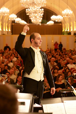 Conductor leading orchestra at Schönbrunn Palace concert with audience in background.