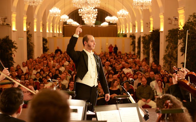 Conductor leading orchestra at Schönbrunn Palace concert with audience in background.