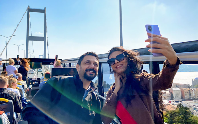 Tourists on Istanbul hop-on hop-off bus with Bosphorus Bridge in background.