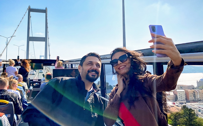 Tourists on Istanbul hop-on hop-off bus with Bosphorus Bridge in background.