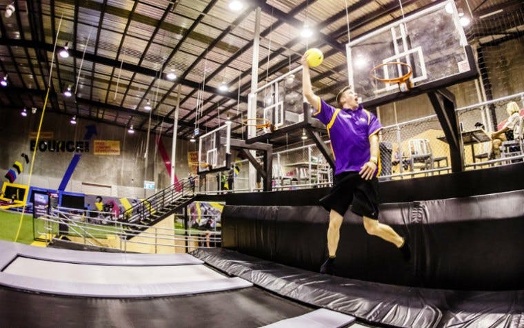 Man jumping on trampoline for a slam dunk in indoor sports arena.