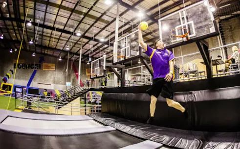 Man jumping on trampoline for a slam dunk in indoor sports arena.