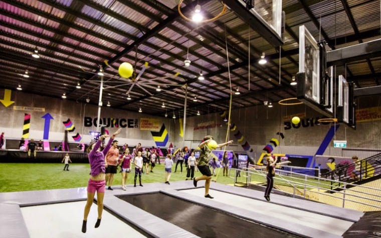 Indoor trampoline park with people playing basketball, featuring multiple hoops and vibrant decor.