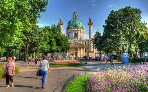 Karlskirche in Vienna with people walking in the garden, location for Vivaldi’s Four Seasons concert.