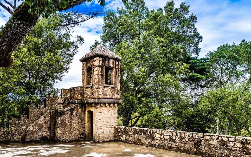 Stone tower at Quinta da Regaleira surrounded by lush greenery, Sintra, Portugal.