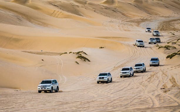 SUVs driving through sand dunes on a Doha half-day desert safari.