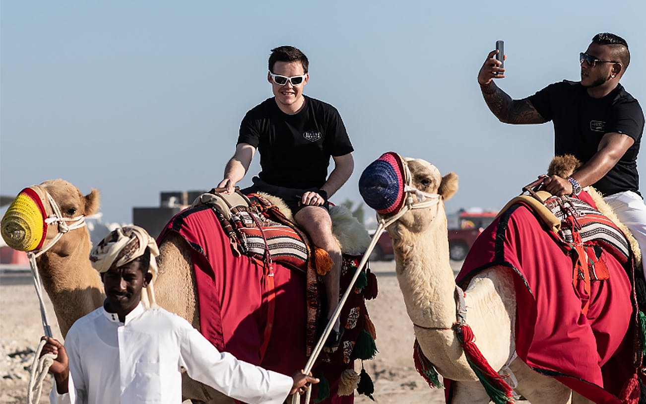 Camel ride during Doha Half-Day Desert Safari with tourists and guide.