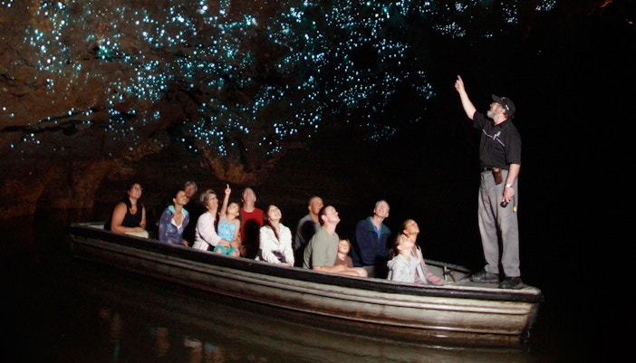 Tour group on boat in Waitomo Glowworm Caves, guide pointing at glowing ceiling.