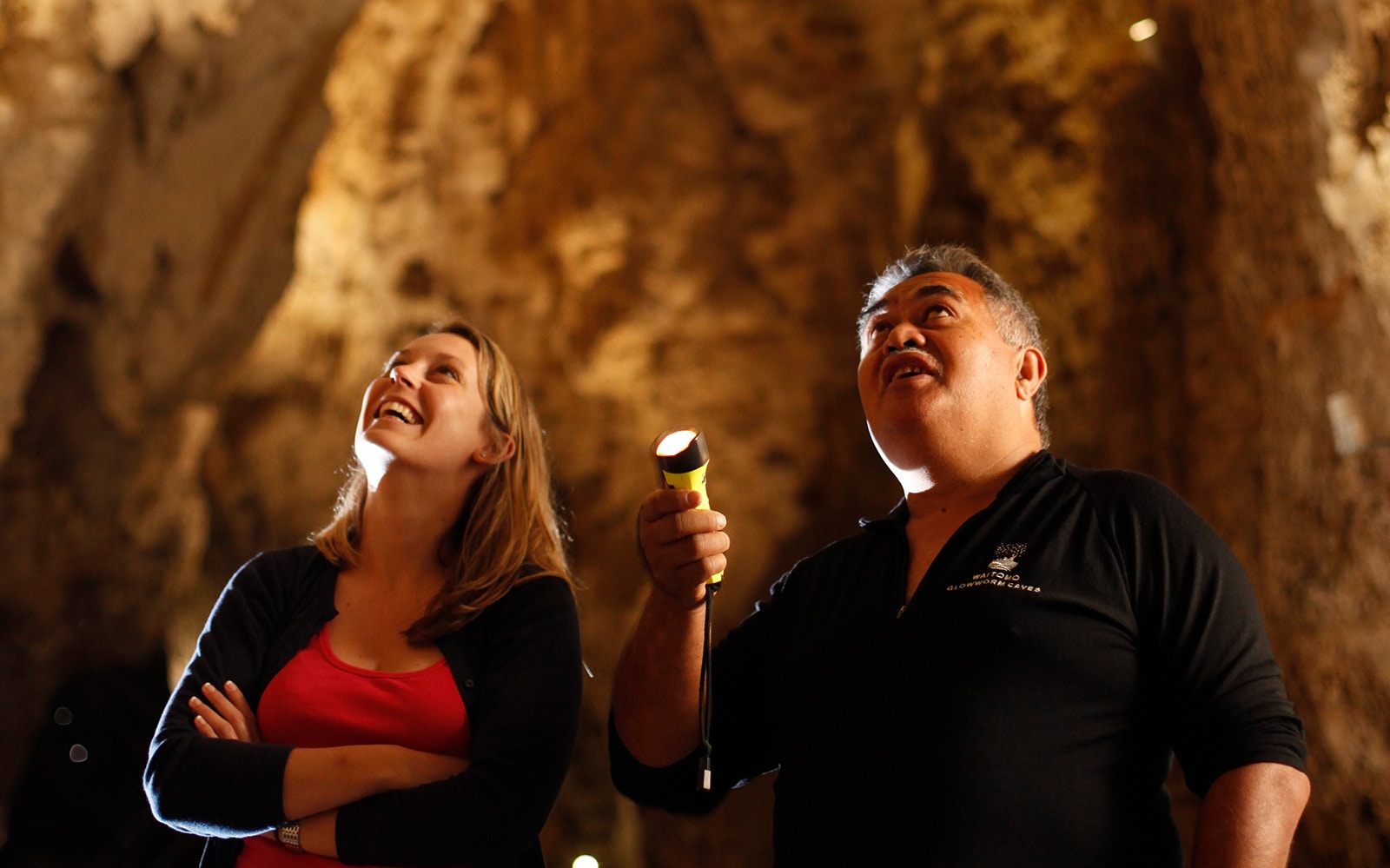 Visitors exploring Waitomo Glowworm Caves with a guide holding a flashlight.