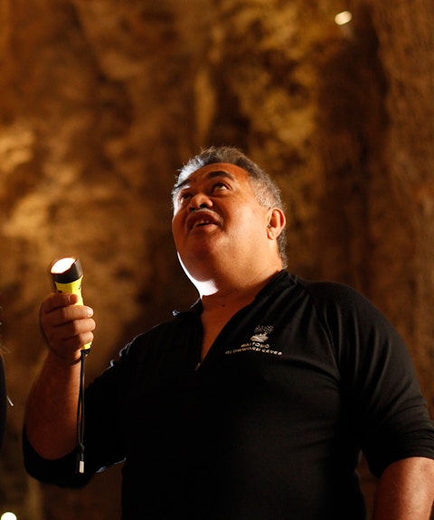 Visitors exploring Waitomo Glowworm Caves with a guide holding a flashlight.